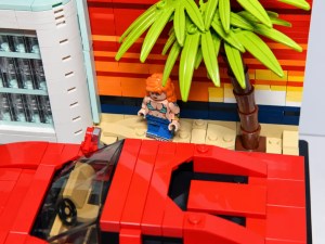 Ein rotes Spielzeugauto und eine kleine Figur vor einer Palme vor einem farbenfrohen Hintergrund.