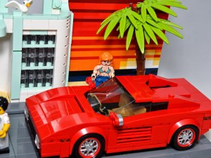 Eine rote Lego-AUTO steht vor einem bunten Hintergrund mit einer Palme, während eine Lego-Figur mit blonden Haaren daneben steht.