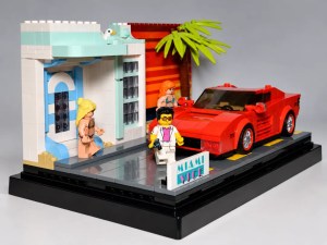 Ein Lego-Diorama mit einem roten Sportwagen, einer stylischen Villa mit Palmbaum und drei Figuren, die vor einem Schild mit der Aufschrift "MIAMI Vice" stehen.