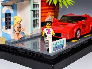 Ein LEGO-Set, das eine Miami-Szenen mit einem roten Sportwagen, einem Mann in einer weißen Jacke und einer Frau neben einem Gebäude darstellt.